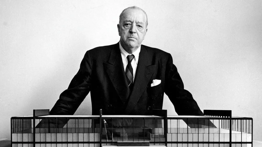 Retrato em preto e branco de Ludwig Mies van der Rohe, arquiteto famoso, com um modelo de edifício à frente.