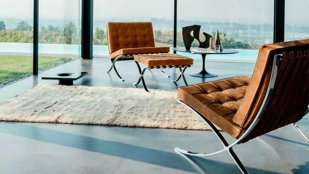 Interior environment with wide windows, burnt cement floor, and classic design chairs with brown leather upholstery, representing furniture in minimalist interior design.