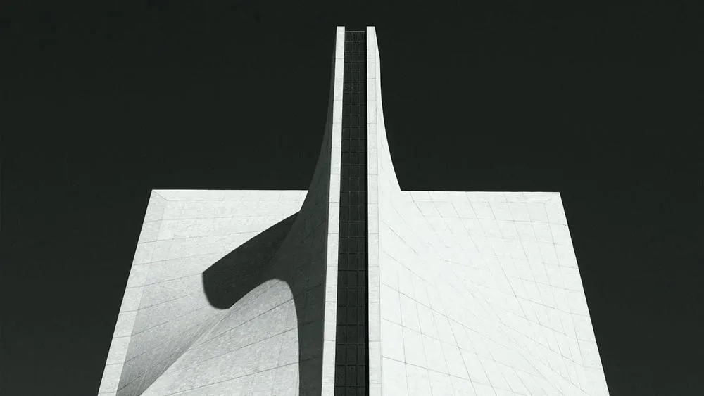 Detail of a modern building facade in white and gray tones, with architectural lines that create shadow and depth, showing the manipulation of spatial perception.