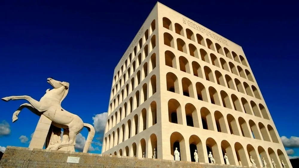 Bottom view of the Palazzo della Civiltà Italiana, a futuristic architecture building with multiple arches, under a blue sky, with a horse statue in the foreground.
