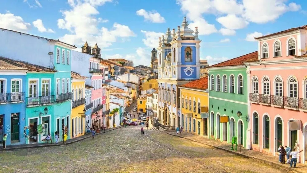 Vista de uma rua colorida no Pelourinho, Salvador, com casas coloniais de diferentes cores e pessoas caminhando.