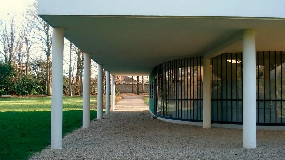 Vista de los pilotis blancos de la Villa Savoye, de Le Corbusier, con la planta baja libre y césped al fondo.