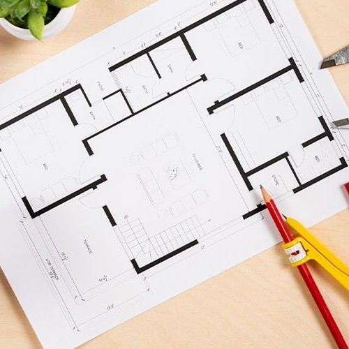 Uma planta baixa arquitetônica, um lápis e uma trena em uma mesa de trabalho, simbolizando o planejamento de um projeto de casa.