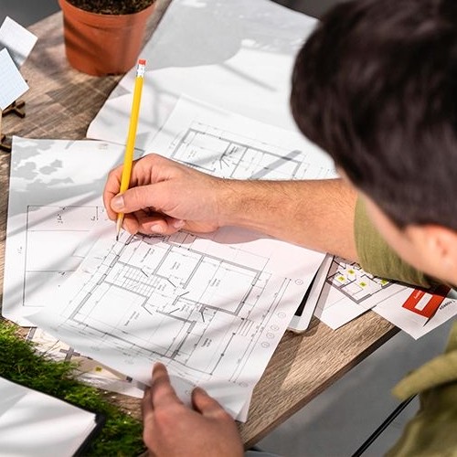 Um profissional de arquitetura desenhando a planta de uma casa em uma mesa.