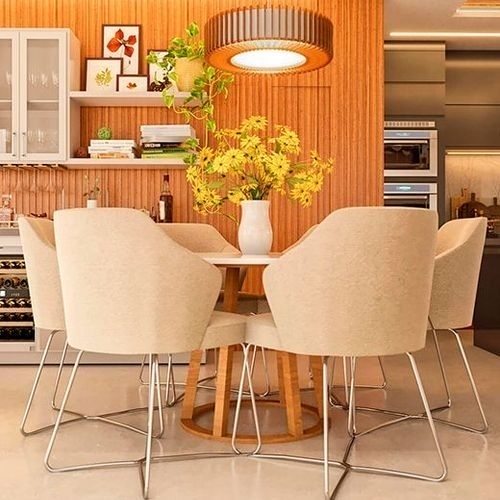 Sala de jantar com mesa redonda e cadeiras estofadas claras, com um arranjo de flores amarelas no centro, criando um ambiente acolhedor.