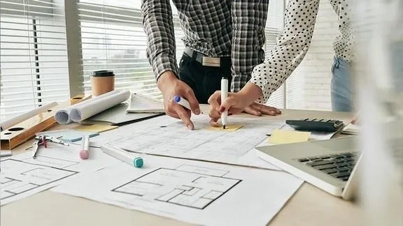 Arquiteto trabalhando em uma prancheta de desenho, com projetos ao fundo.