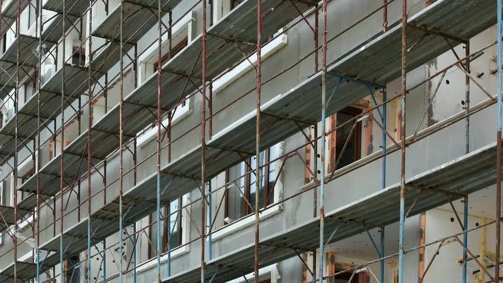 Detalle de un andamio frente a un edificio en reforma, con ventanas y revestimientos siendo trabajados, ilustrando la diferencia entre reforma y retrofit.