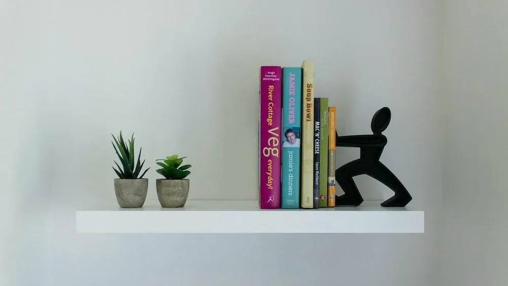 White floating shelf with books and plants, and a creative doorstop, ideal for decorating a rented house.