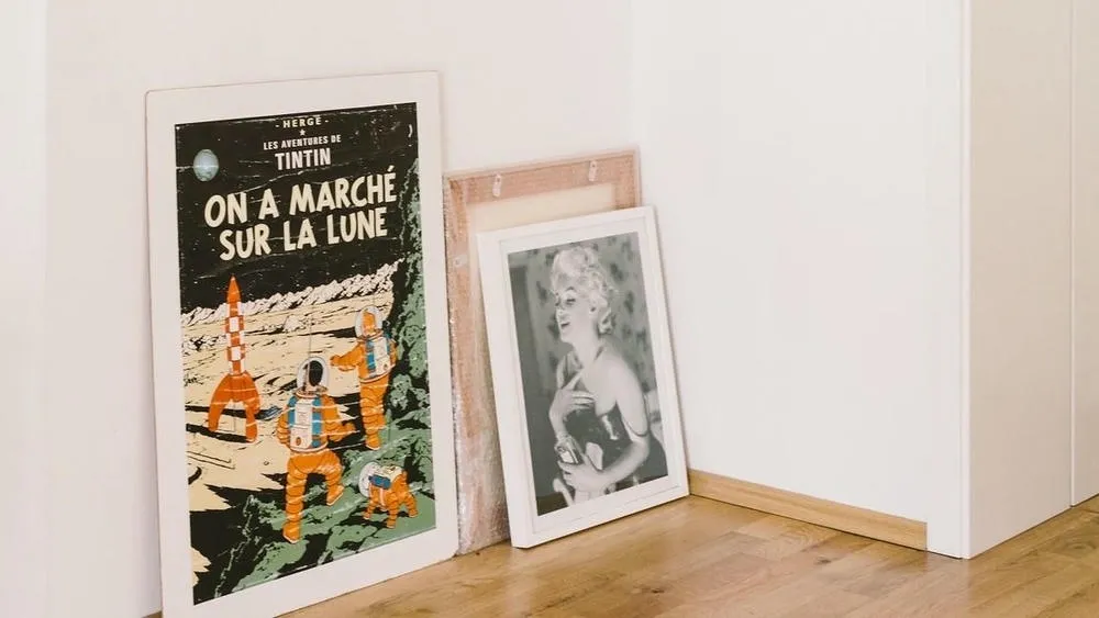 Frames and posters leaning on the floor, next to a white wall, suggesting a way to decorate a rented house without drilling the wall.