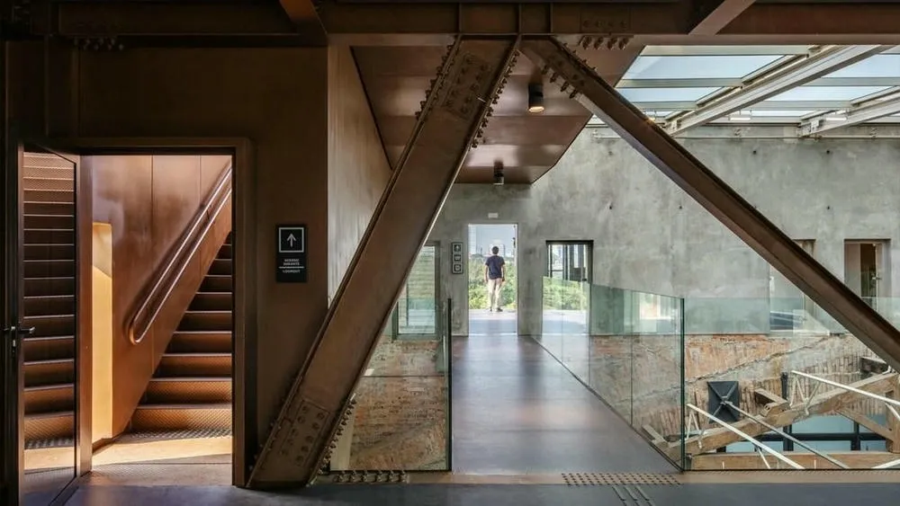 Interior of a building with exposed metallic structures, brick and concrete walls, and a corridor with glass doors, illustrating the modernization and functionality of retrofit.