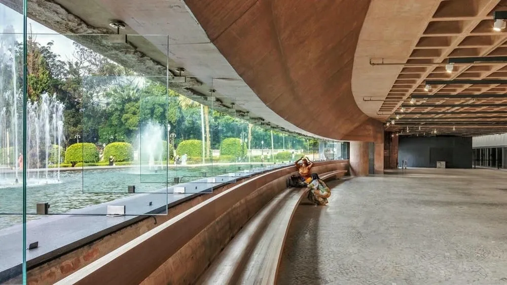 View of a modern corridor with concrete walls and a large glass window overlooking a fountain and vegetation, representing the integration of sustainability in retrofit projects.