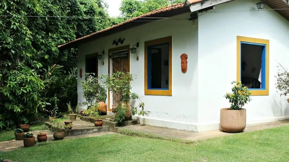 Rustic and simple country house, with white walls, windows with colorful frames, and potted plants at the entrance.