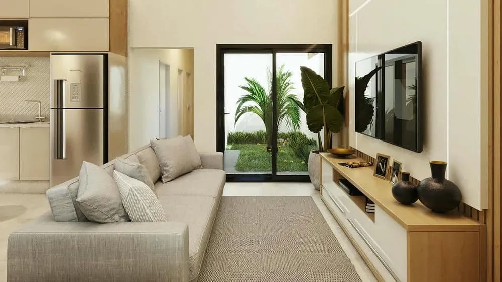 Sala de estar con sofá gris, panel de TV de madera y plantas grandes al lado de la ventana, enfatizando el uso de plantas en la decoración natural.