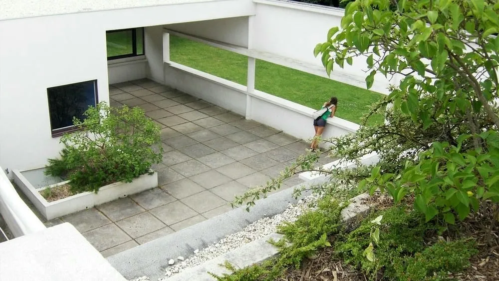 Mujer observando el jardín en la terraza de la Villa Savoye, destacando la integración de la naturaleza en la cima del edificio.