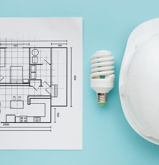 A printed floor plan next to a fluorescent lamp and a white safety helmet, on a light blue background.